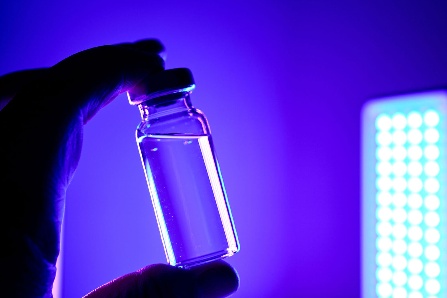 Mano con guante sostiene un vial iluminado con luz azul en una investigación de biología química sobre GPCR intracelulares en células cardiacas.